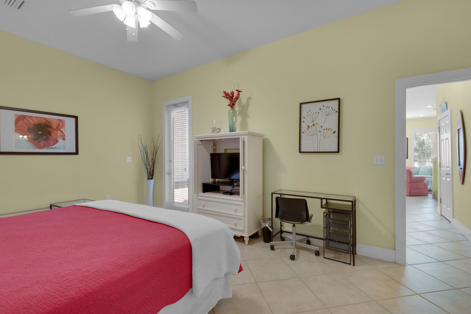 A bedroom with a bed, a desk, a chair, a TV, and a door leading to another room.