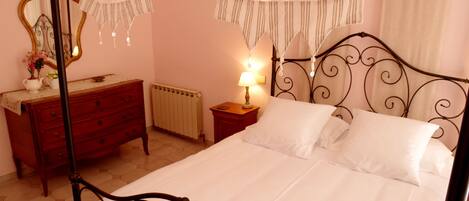 A bedroom with a four-poster bed, a wooden dresser, a nightstand with a lamp, and a mirror on the wall.