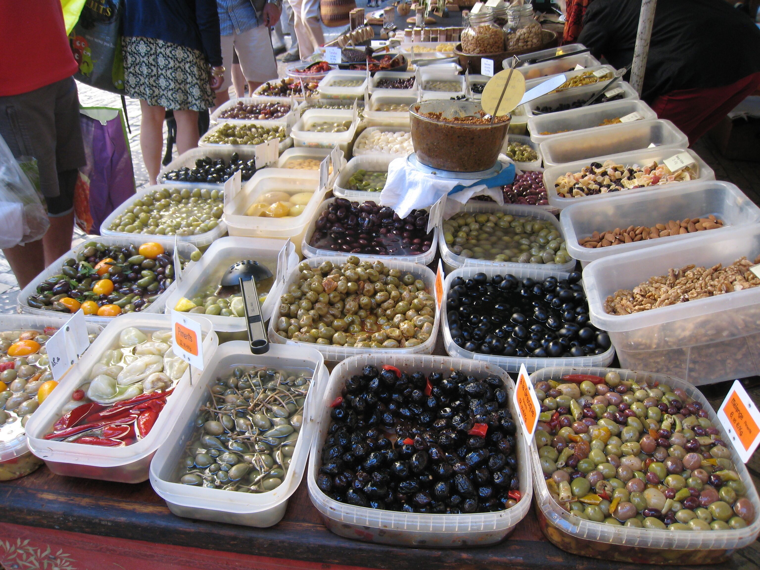 Un assortimento di olive e noci esposto in contenitori trasparenti a una bancarella di mercato.