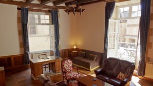 Un salón acogedor con suelo de madera, un sofá, una butaca, una mesa de centro y una ventana con cortinas.