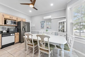 A kitchen with wooden cabinets, a white island with chairs, a ceiling fan, and a window with blinds. - *3rd to Beach*BIG DISCOUNTS Summer Weeks *CleanUPDTDVictorian*Across VeteranPrk (Beach Haven)