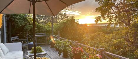 A wooden deck with outdoor furniture, potted plants, and a large umbrella.