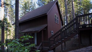 A wooden cabin with a staircase leading to a porch, surrounded by trees.