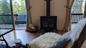 A cozy room with a wooden bench, a fluffy white cushion, a black and white patterned rug, and a black wood-burning stove.