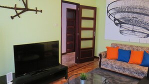 Una sala de estar con televisor de pantalla plana, un sofá con cojines de colores, una mesa de centro de vidrio y una puerta con marco de madera.