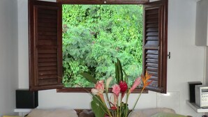 A room with a sofa, a white vase with flowers, and a window with open shutters. - Exceptional Seaview - All The Comforts You Need (Schoelcher)