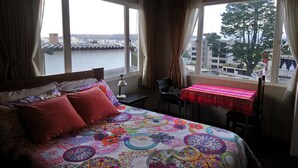 A bedroom with a bed, a chair, a table, and large windows with curtains.