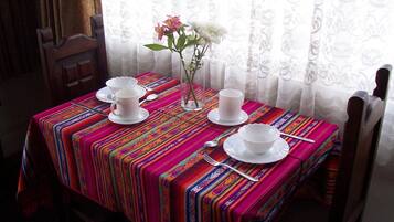 Une table dressée avec des tasses et des soucoupes blanches, un vase rempli de fleurs, le tout recouvert d’une nappe rayée aux couleurs vives.