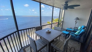 A balcony with a table and chairs, overlooking a body of water and a distant island.