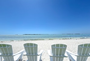 A beach with white chairs facing the ocean, clear skies, and calm water. - Sanibel Harbour Resort Bay View Tower 535: Beachfront vacation retreat with stunning sunset views. (Fort Myers)