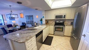 A modern kitchen with white cabinets, a granite countertop, stainless steel appliances, and pendant lighting.