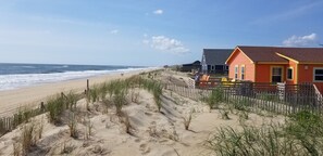 A beach with a wooden fence, a sandy path, and a building with a red roof.