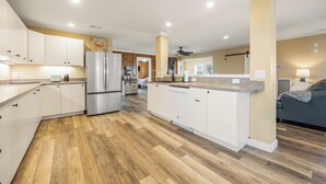 Eine moderne Küche mit weißen Schränken, einem Edelstahl-Kühlschrank, Holzboden und einem Deckenventilator.