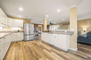 Eine moderne Küche mit weißen Schränken, einem Edelstahl-Kühlschrank, Holzboden und einem Deckenventilator.