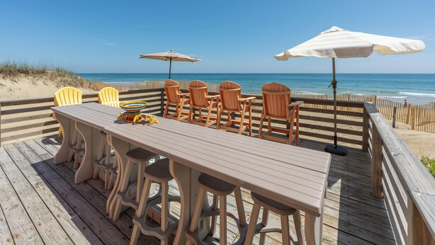 Eine Holzterrasse mit Tisch und Stühlen mit Blick auf den Strand.