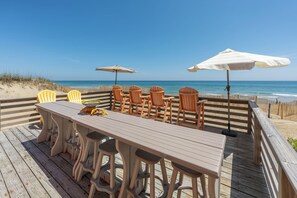 Une terrasse en bois avec une table et des chaises, donnant sur la plage.