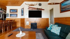 A cozy living room with wooden walls, a fireplace, a mounted TV, and a green sofa. - Misty Mountain -  September Special Now Available (Jindabyne)