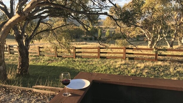 A picnic table with a wine glass and a plate, surrounded by a wooden fence and trees. - Misty Mountain -  September Special Now Available (Jindabyne)