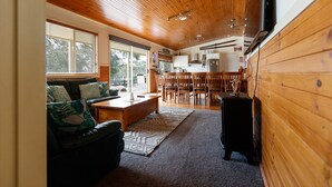 A spacious living area with a wooden ceiling, a sofa with patterned cushions, a coffee table, and a dining area with chairs and a table. - Misty Mountain -  September Special Now Available (Jindabyne)