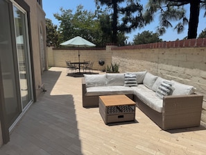 An outdoor patio with a wicker sofa, a wooden coffee table, a dining table with chairs, and a barbecue grill. - Modern Tustin Home  Tesla Universal EV  30+ Days (Tustin)