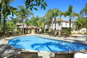 A swimming pool surrounded by palm trees and lounge chairs, with a clear blue sky above. - Modern Tustin Home  Tesla Universal EV  30+ Days (Tustin)