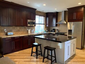 A modern kitchen with dark wood cabinets, a central island with stools, a stainless steel refrigerator, and a microwave. - Modern Tustin Home  Tesla Universal EV  30+ Days (Tustin)
