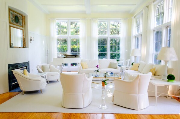 A spacious living room with white furniture, large windows, and a fireplace.
