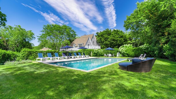 A swimming pool with lounge chairs and a dining area, surrounded by lush greenery and a large house in the background. - Stunning House: Tennis & Pool in Southampton Estate section (Southampton)