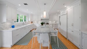 A modern kitchen with white cabinetry, a marble island, and a large window providing natural light. - Stunning House: Tennis & Pool in Southampton Estate section (Southampton)