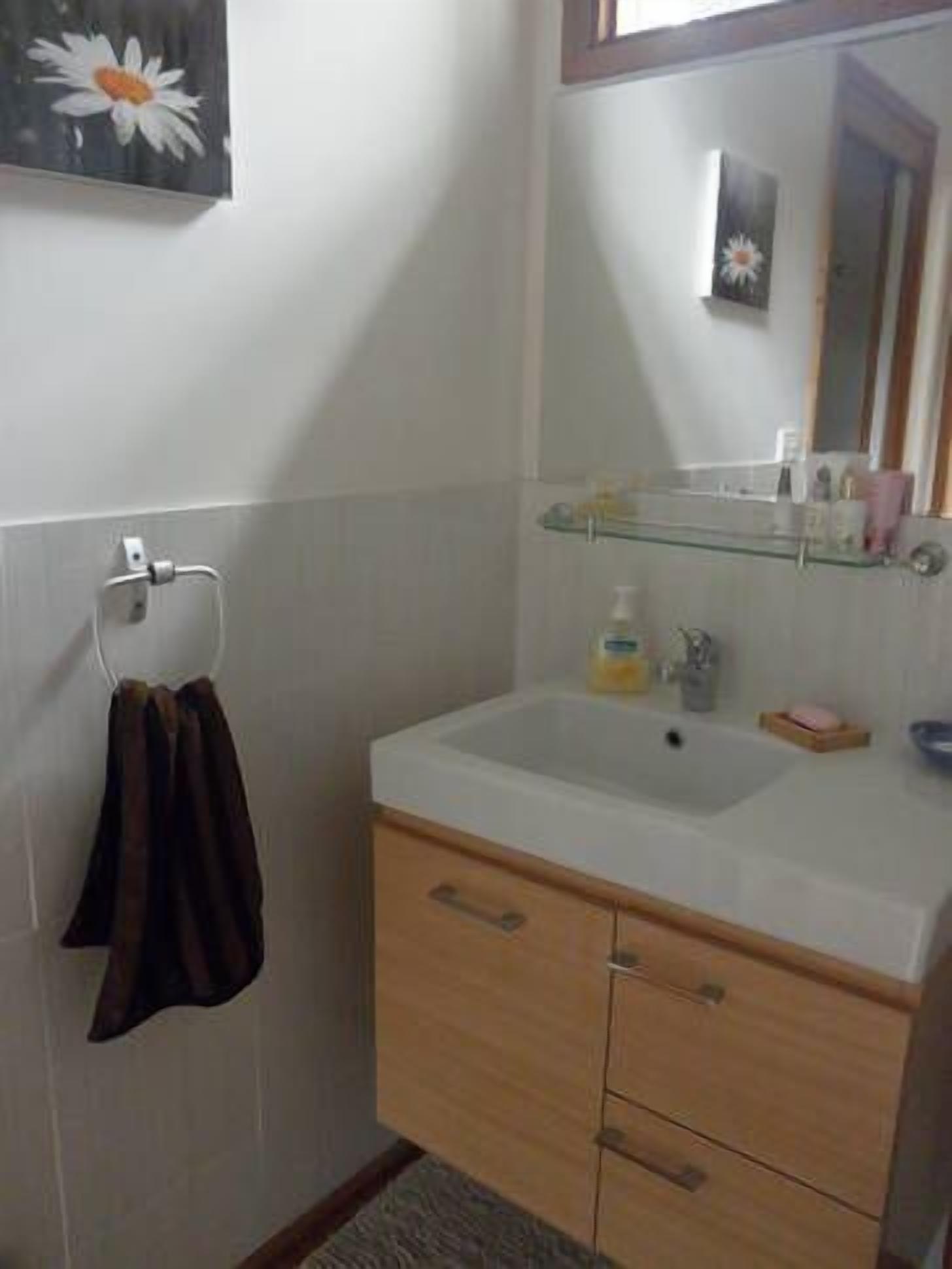 A bathroom with a white sink, wooden cabinet, and a towel hanging on a rack.