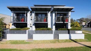 A modern three-story residential building with balconies, a flat roof, and a paved driveway. - Unit 3 - Modern 2BR Apartment on Huskisson Main Street By Nautilus Apartments Je (Huskisson)