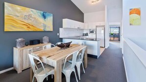 A modern kitchen with white cabinets, a central island, and a dining area with a wooden table and white chairs. - Unit 3 - Modern 2BR Apartment on Huskisson Main Street By Nautilus Apartments Je (Huskisson)