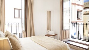A hotel room with a bed, a bedside table with a lamp, a window with a view of buildings, and a balcony with a railing. - Beautiful And Central House For Up To 8 Guests (Cordoba)