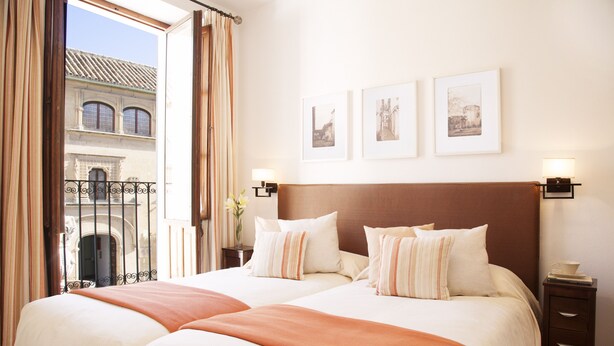 A hotel room with two beds, a view of a building through a window, and three framed pictures on the wall. - Beautiful And Central House For Up To 8 Guests (Cordoba)