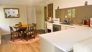 A modern kitchen with a dining area, featuring a wooden dining table, chairs, a kitchen island, and a built-in oven.