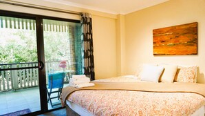 A bedroom with a bed, a painting, and a view of a balcony with a chair and a table.