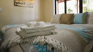 A neatly made bed with rolled white towels, a patterned blanket, and a decorative throw.