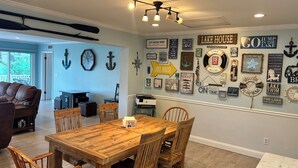 A dining area with a wooden table and chairs, a ceiling light fixture, and various wall decorations including nautical-themed signs and an anchor.