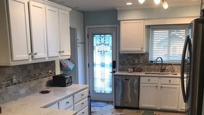 A kitchen with white cabinets, a stainless steel refrigerator, a dishwasher, and a large island with stools.