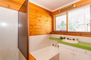 A bathroom with wooden walls, a window with blinds, a sink with green countertop, and a bathtub.
