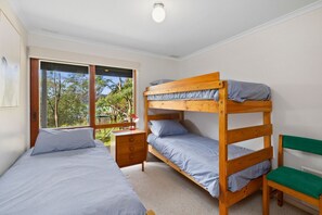 A bedroom with two bunk beds, a desk, a chair, and a window with a view of trees.