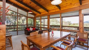 A wooden interior with a large dining table, chairs, and a sofa with cushions. - La Tienda (Lorne)