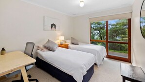 A bedroom with two beds, a desk, and a window with a view of trees. - La Tienda (Lorne)