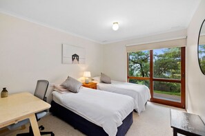 A bedroom with two beds, a desk, and a window with a view of trees.