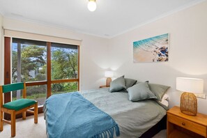 A bedroom with a bed, a chair, a nightstand, a lamp, and a painting. - La Tienda (Lorne)