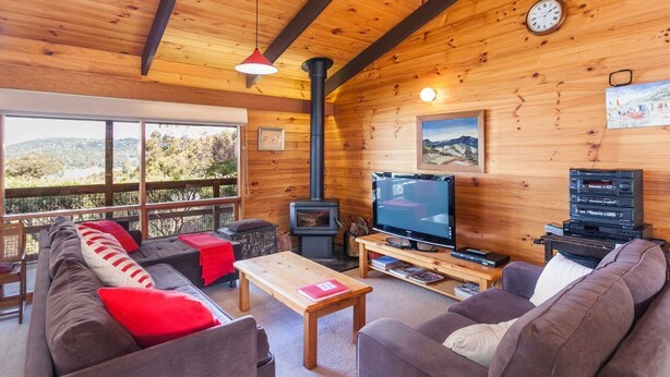 A cozy cabin interior with a sofa, television, and a fireplace. - La Tienda (Lorne)