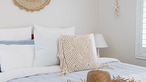 A neatly made bed with white and striped bedding, a crocheted throw, and a woven basket on the side. - Kalinda (Mollymook Beach)