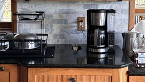 Une cuisine avec des étagères en bois où sont rangés de la verrerie et des tasses, une machine à café et un égouttoir à vaisselle.