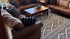 Un salon avec un canapé en cuir marron, une table basse en bois et un tapis à motifs.