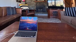 Un salon avec une cheminée en pierre, un téléviseur et un ordinateur portable posé sur une table basse en bois.